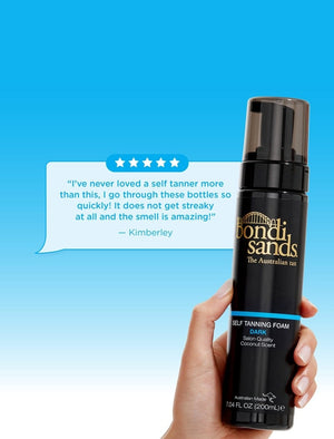 A hand holds a bottle of BondiSandsEU Self Tanning Foam Dark against a blue backdrop, while a customer review above highlights its bronzed tan results, streak-free application, and pleasant scent.