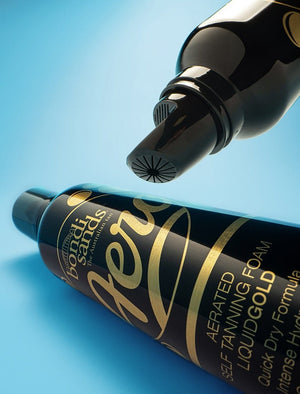 A close-up of two black BondiSandsEU Aero Self Tanning Foam Liquid Gold bottles with gold lettering, one upright displaying the nozzle and one lying down on a blue background—ideal for a long-lasting natural tan.