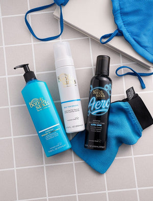Three BondiSandsEU tanning products, including Aero Self Tanning Foam Ultra Dark, are displayed on gray tiles with a blue mitt and swimsuit, promising a flawless bronzed tan.