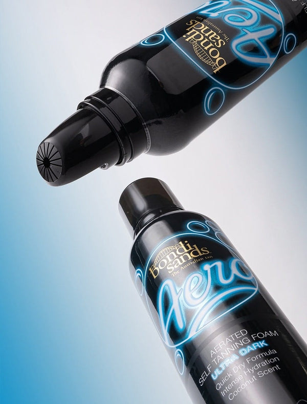 Two black bottles of BondiSandsEU Aero Self Tanning Foam Ultra Dark are shown on a blue gradient background—one upright displaying the label, the other tilted to reveal the pump dispenser for a flawless bronzed tan.