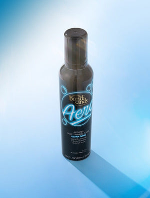 A bottle of BondiSandsEU Aero Self Tanning Foam Ultra Dark stands upright on a blue gradient background with a soft shadow, promising an ultra dark, flawless bronze tan.