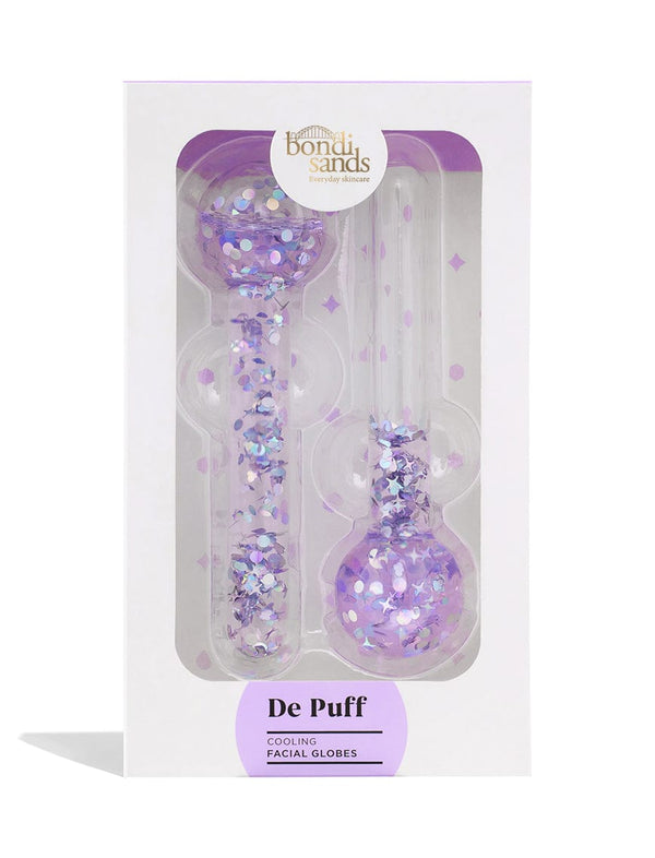 The BondiSandsEU De Puff Cooling Facial Globes boxed set includes two clear wands with purple glitter and confetti, designed to reduce puffiness, all presented in sleek clear plastic packaging.