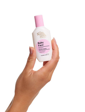 A hand holds a BondiSandsEU Baby Face Retinol Serum bottle with a pink cap and label, set against a white background—ideal for targeting fine lines and promoting youthful-looking skin.