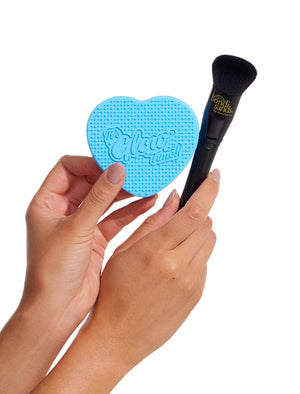 Two hands hold the BondiSandsEU Self Tan Contour Kit, featuring a blue heart-shaped cleaning pad and a black makeup brush—ideal for flawless bronzing or contouring—set against a clean white background.