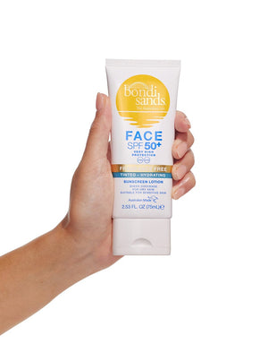 A hand holds a tube of BondiSandsEU SPF 50+ Fragrance Free Hydrating Tinted Face Lotion, 75ml. The white packaging with gold, blue, and orange accents highlights this daily sun protection face lotion.