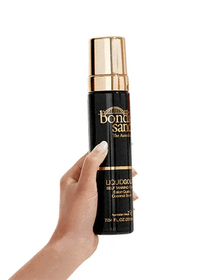 A hand dispenses mousse from a black and gold BondiSandsEU Glow & Go Bundle bottle against a white background, giving that perfect golden glow.
