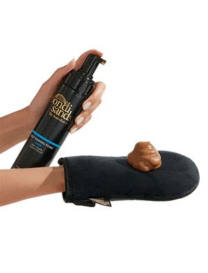 A hand pumps BondiSandsEU Dark Foam Gift Set onto a black Application Mitt, ready for use, against a white background.
