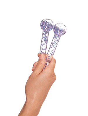 A hand holds two BondiSandsEU De Puff Cooling Facial Globes with iridescent glitter, set against a white background. These facial massage tools have handles and help reduce puffiness.