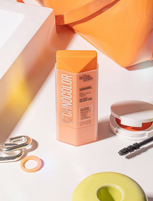 A bottle of BondiSandsEU Technocolor Caramel Self Tanning Face Serum sits on a white surface among mascara, a ring, and pastel containers, emphasizing its natural tan promise for deep skin tones.