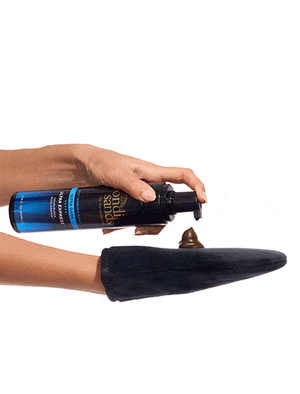 A hand dispenses Bondi Sands Europe Ultra Express Self Tanning Foam onto a black tanning mitt held by another hand, set against a white background.