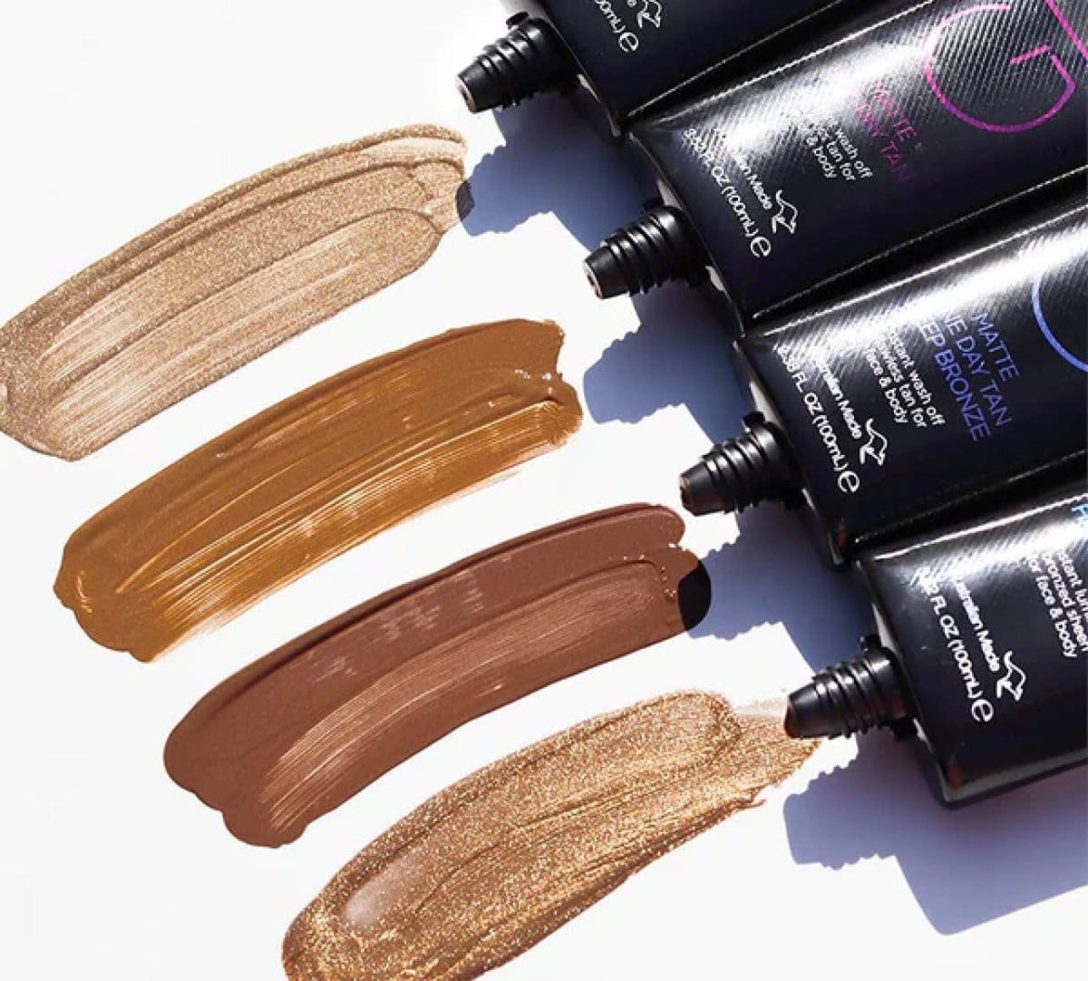 Four tubes of BondiSandsEU GLO Matte One Day Tan are squeezed onto a white surface, showing creamy, glossy textures in shades from light gold to deep brown—ideal for achieving a natural-looking or one day tan.