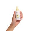 A hand holds a bottle of BondiSandsEU Sunny Daze Hydrating SPF 50+ Face Fluid Drops with a yellow dropper cap, shown against a white background.