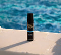 A BondiSandsEU Dark Self Tanning Foam Bundle sits on a white surface against a blurred, vibrant blue water backdrop, offering a natural glow and flawless self tan.