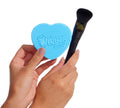 A person holds the BondiSandsEU Self Tan Contour Kit—featuring a blue heart-shaped cleaner and contour brush—against a white background, ideal for creating a flawless bronzed glow.