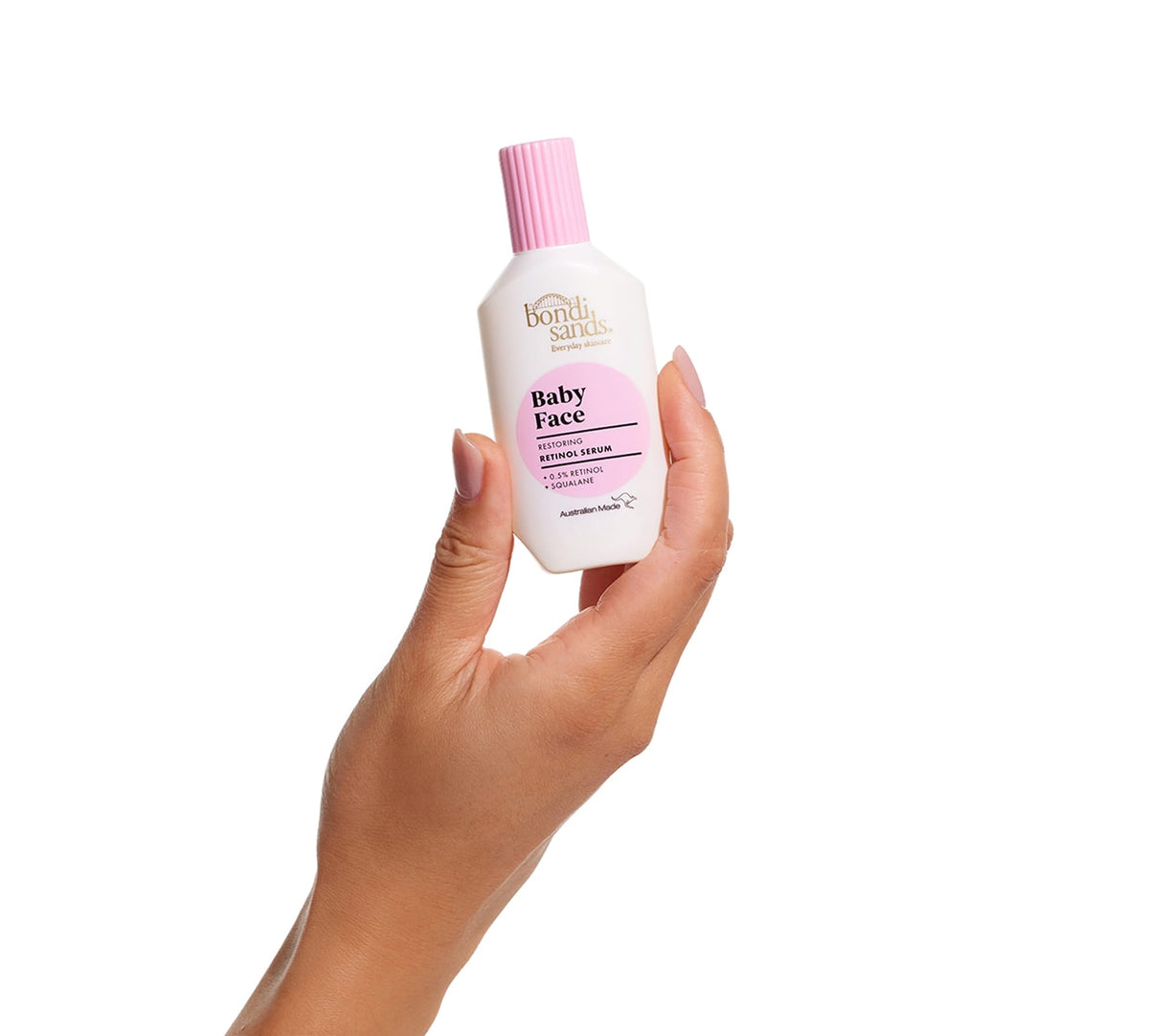 A hand holding a white bottle with a pink cap labeled BondiSandsEU Baby Face Retinol Serum, designed to reduce fine lines for youthful-looking skin, against a plain white background.