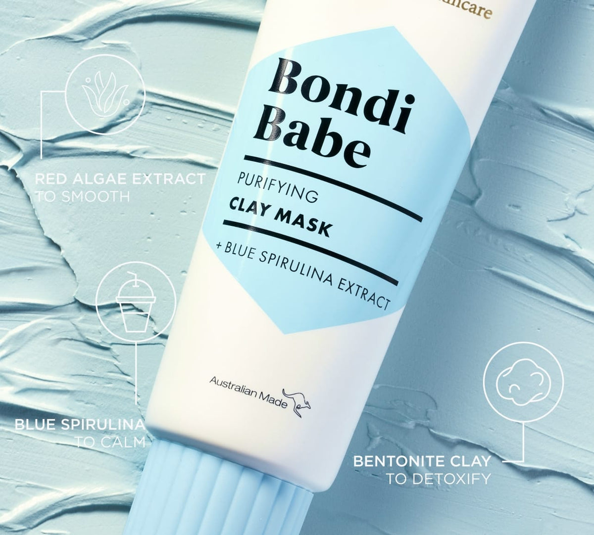 A tube of BondiSandsEU Bondi Babe Clay Mask rests on blue clay, featuring red algae, blue spirulina, and bentonite clay to detoxify skin and reveal a glowing, healthy radiance.