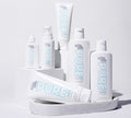 Several white bottles and tubes of BondiSandsEU’s Pure Self Tanning Sleep Mask are neatly displayed on a white tray and blocks with light blue lettering, set against a clean white background.