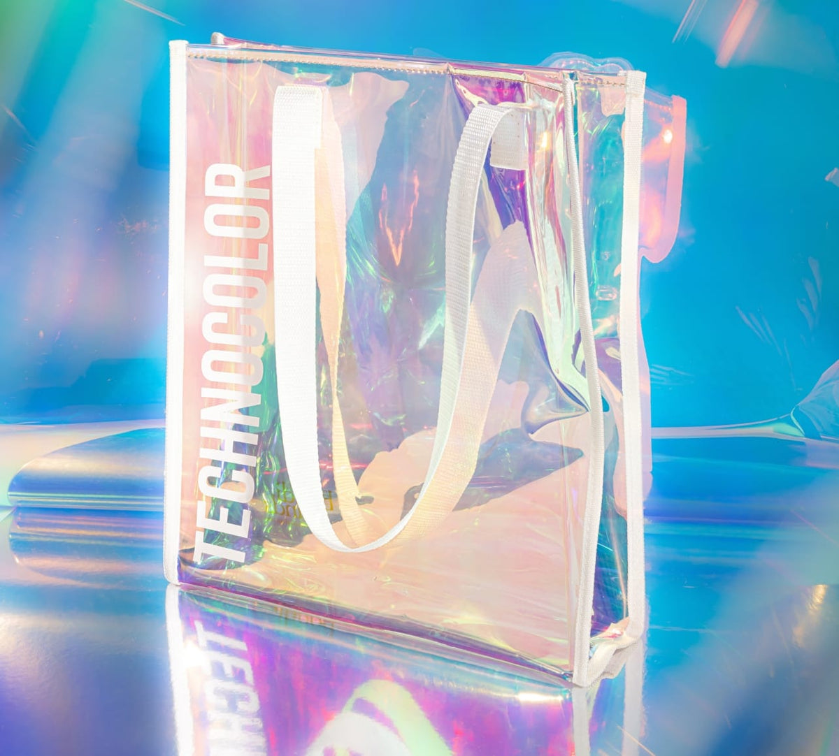 The BondiSandsEU Technocolor Tote Bag features a transparent holographic design with white handles, "TECHNICOLOR" printed vertically in bold white on the front—an eye-catching, limited edition accessory.
