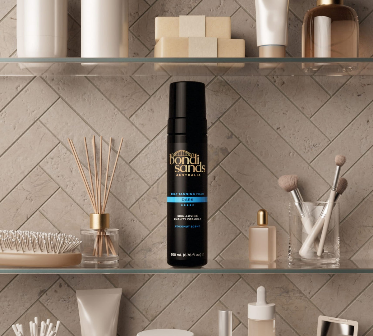A BondiSandsEU Dark Foam Gift Set rests on a glass shelf, surrounded by makeup brushes, skincare bottles, and beauty products against a tiled bathroom wall.