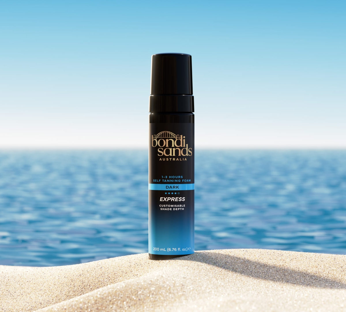 A BondiSandsEU Express Self Tanning Bundle stands upright on sandy beach with the ocean and clear blue sky in the background.