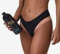 A person in black underwear holds a large bottle of BondiSandsEU Salon Solution Ultra Dark, displaying a visible tan line on their hip against a plain white background—ideal for achieving a salon-quality tan at home.