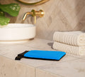 The BondiSandsEU Exfoliation Mitt sits on a marble counter beside folded white towels, with a white sink, gold faucet, and green plant in the background—perfect for achieving a streak-free glow.