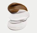 A smear of BondiSandsEU Everyday Gradual Tanning Milk’s rich brown formula over glossy white cream on a plain white background, ideal for achieving a radiant daily glow.