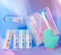 Four bottles of BondiSandsEU Magenta Technocolor 1 Hour Express Self Tanning Foam, a turquoise mitt, an iridescent tote, and a matching cosmetic pouch are arranged on a pastel pink and blue background—ideal for olive to deep skin tones.