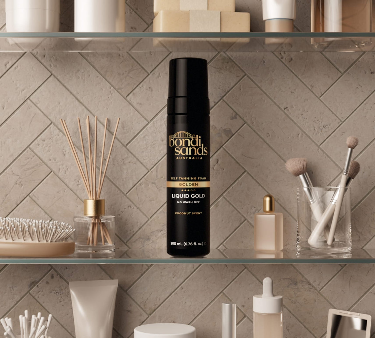 A BondiSandsEU Liquid Gold Self Tanning Routine Bundle rests on a bathroom shelf alongside an exfoliating mitt, makeup brushes, skincare bottles, and toiletries against a tiled wall.