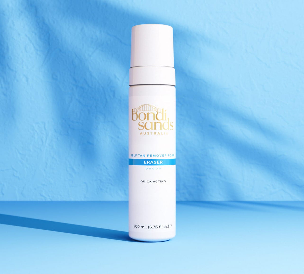 A white and blue bottle of BondiSandsEU Self Tan Eraser stands upright on a blue surface, casting a shadow against a textured blue background.