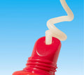A close-up of a red BondiSandsEU Watermelon SPF 50+ Lip Balm releasing a swirl of white cream with a clear blue sky in the background.