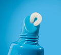 A close-up of a BondiSandsEU Vanilla SPF 50+ Lip Balm, with its cap off and a swirl of white balm emerging from the blue tube's nozzle against a blue background.