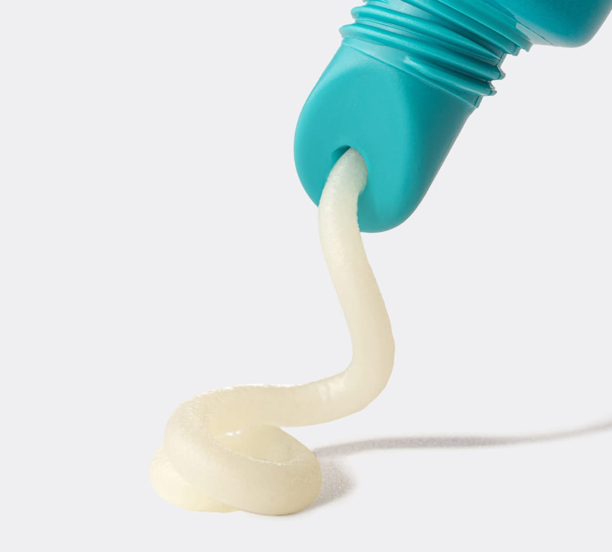 A close-up of BondiSandsEU's Vitamin E Toasted Coconut Lip Balm in a teal tube dispensing thick, white balm in a swirl onto a white surface—ideal for those seeking nourishing Vitamin E care.