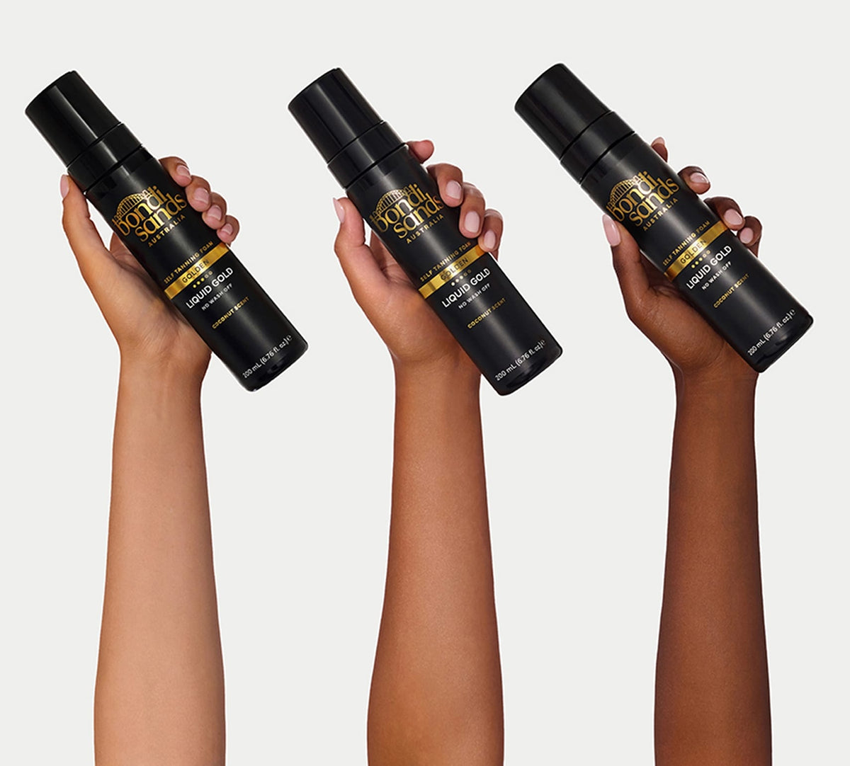 Three hands of different skin tones hold a black BondiSandsEU Liquid Gold Self Tanning Foam bottle, highlighting its golden glow benefits against a plain white background.