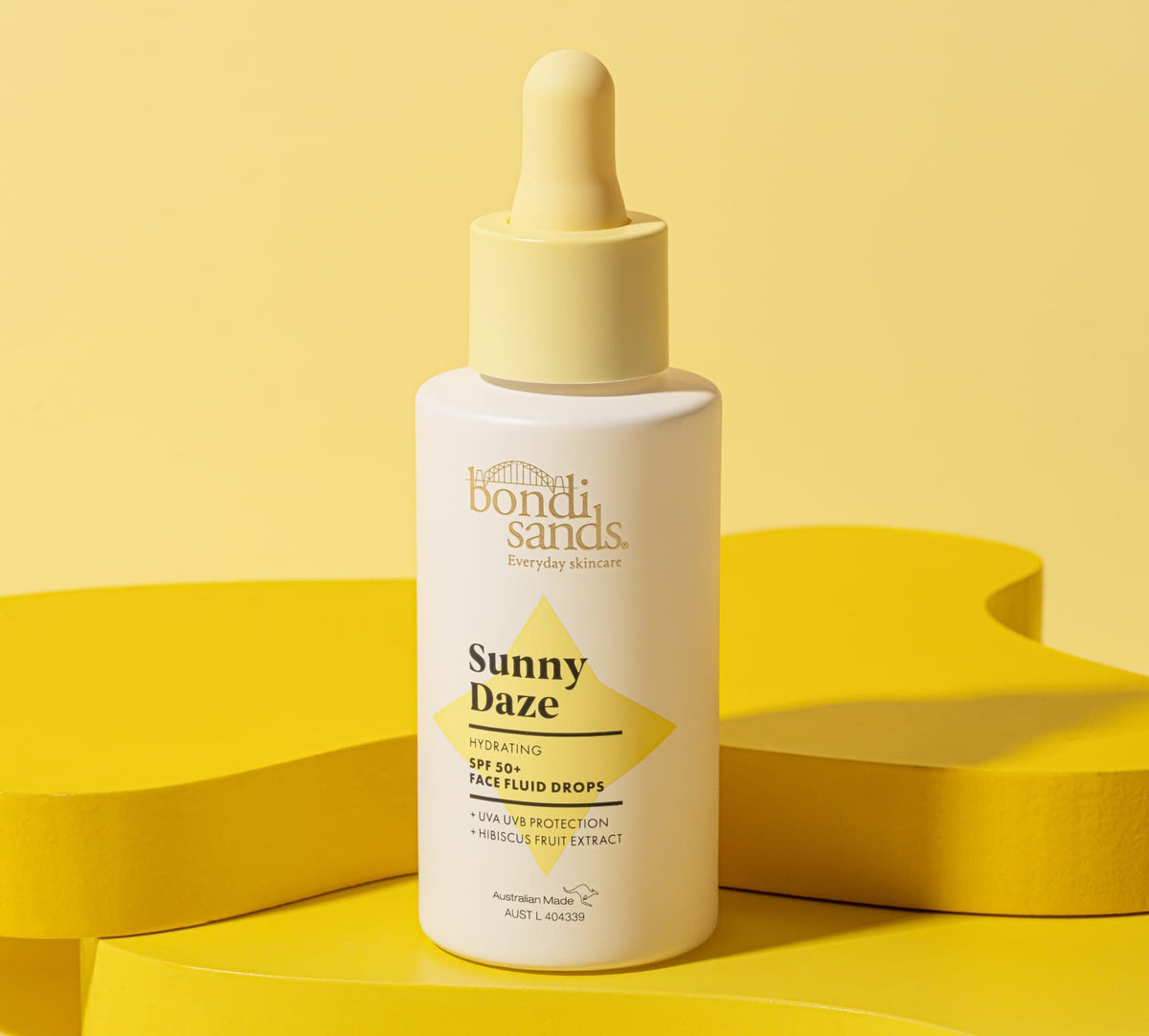 A bottle of BondiSandsEU Sunny Daze Hydrating SPF 50+ Face Fluid Drops with a yellow cap and label accents stands on a bright yellow background, creating a clean, summery vibe.