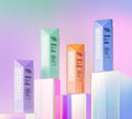 Four rectangular bottles of BondiSandsEU Sapphire Technocolor Self Tanning Face Serum in magenta, green, orange, and blue stand on translucent blocks against a pastel gradient background, each with a white "TECHNICOLOR" label.
