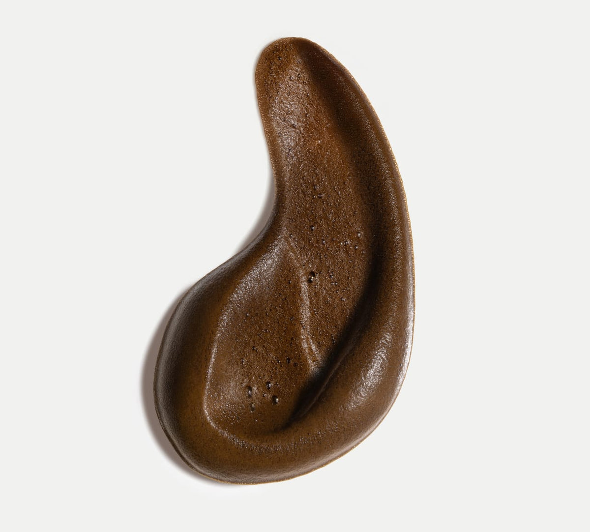 A brown, ear-shaped substance with a smooth, air-bubbled texture is shown on white, resembling the sun-kissed finish from the Bondi Sands Europe Ultra Express Self Tanning Foam & Application Mitt Bundle.