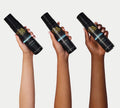 Three hands of different skin tones each hold a black bottle of BondiSandsEU Light/Medium Self Tanning Foam against a plain, light background, highlighting the secret to achieving a natural glow for every complexion.