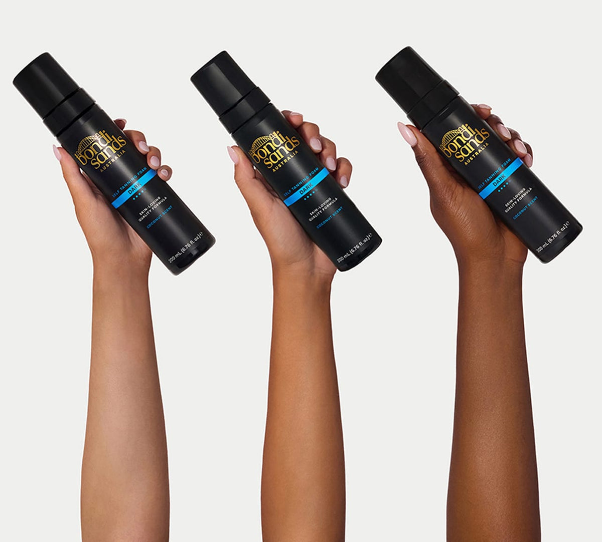 Three hands of varying skin tones each hold a black bottle of BondiSandsEU Dark Self Tanning Foam, featuring gold and blue labels, set against a plain light background.