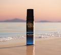 Bondi Sands Europe Ultra Express Self Tanning Foam stands upright on wet sand by the shoreline, with gentle waves, calm water, and distant mountains at sunset—ideal for fast tanning results.