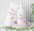 The BondiSandsEU Tropical Rum Body Wash sits on a white surface with a pink dish and green plants, set against crisp white tiles.