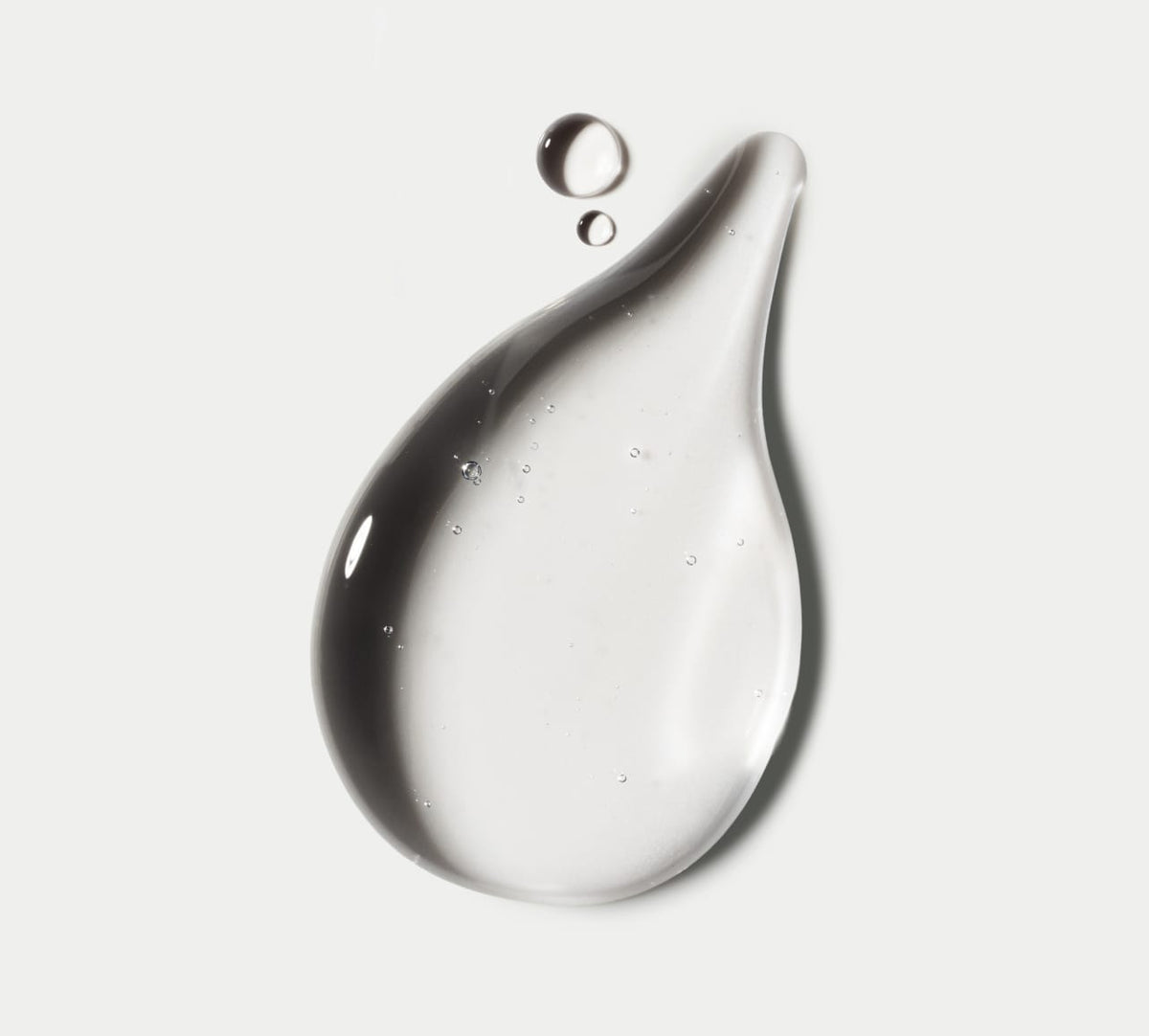 A large, glossy droplet—evoking self-tan drops—with tiny bubbles sits beside two smaller drops against white. Showcasing the Glow Head to Toe Bundle by BondiSandsEU.