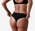 A person with a bronzed glow from BondiSandsEU Light-Medium Salon Solution 1L Duo, wearing black bra and underwear, is shown from the back adjusting their waistband against a plain white background.