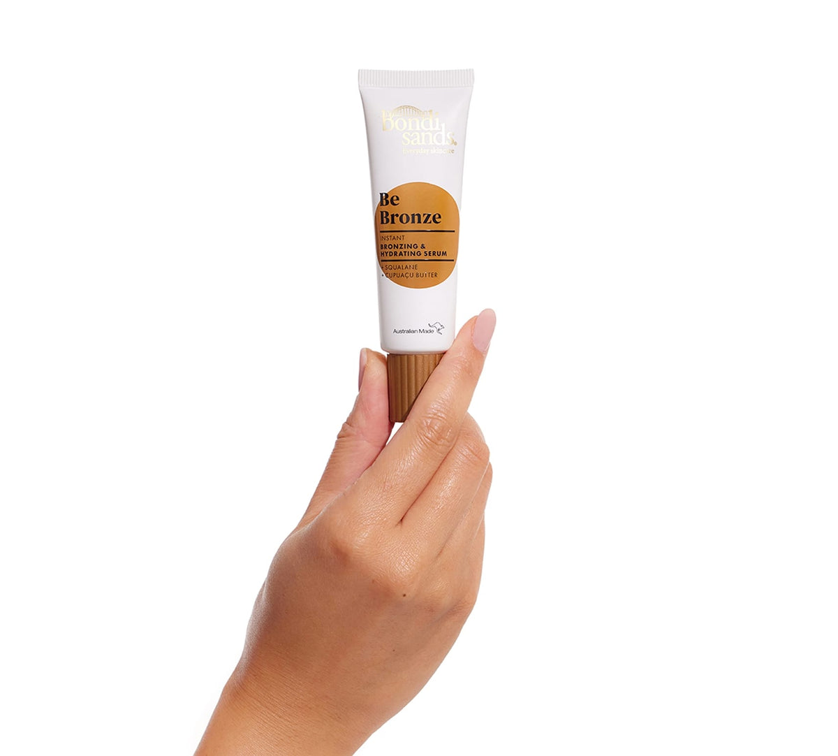 A hand holds a tube of BondiSandsEU Be Bronze Instant Bronzing & Hydrating Serum, a glow-boosting formula for a radiant, bronzed complexion, set against a plain white background.