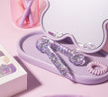 Two sparkly, clear De Puff Cooling Facial Globes by BondiSandsEU rest on a lavender tray near a wavy mirror, with a pink spiral hair tie, makeup brushes in a pink cup, and a Benefits Smile box—ideal for de-puffing and lymphatic drainage.