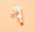 A tube of BondiSandsEU Eye Spy Vitamin C Eye Cream with an orange cap rests on a peach background beside a swirl of cream, designed to brighten the under-eye area and reduce dark circles.