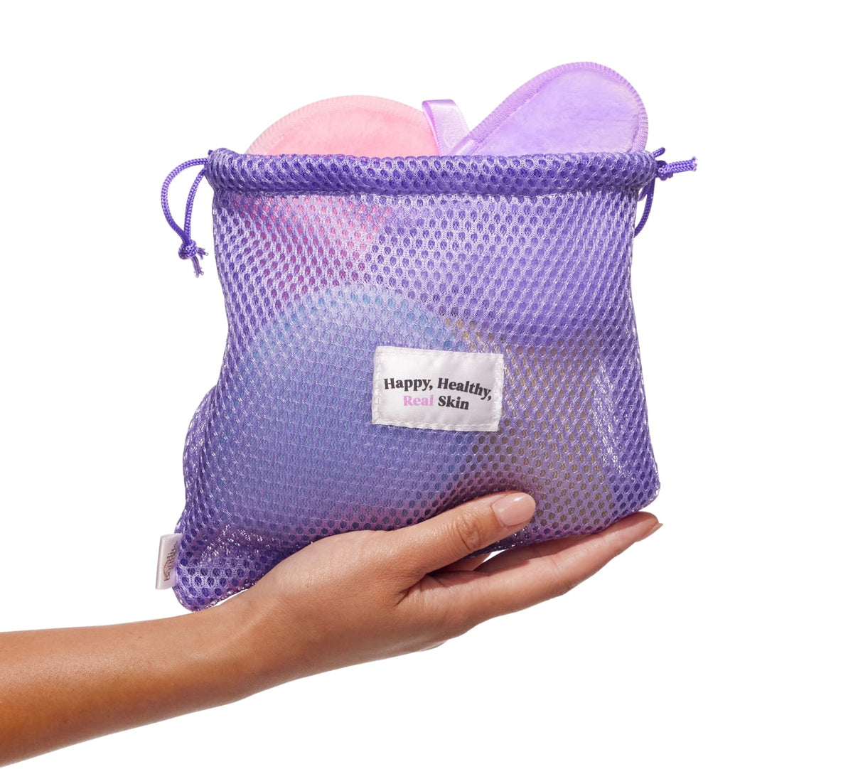 A hand holds a purple mesh drawstring bag labeled "Happy. Healthy. Real Skin," with BondiSandsEU Squeaky Clean Reusable Makeup Pads in pink and purple inside, shown against a white background.