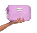 A hand holds the BondiSandsEU Everyday Skincare Cosmetic Bag—a light purple, textured zippered pouch with a white label—perfect as a travel-friendly skincare bag against a white background.
