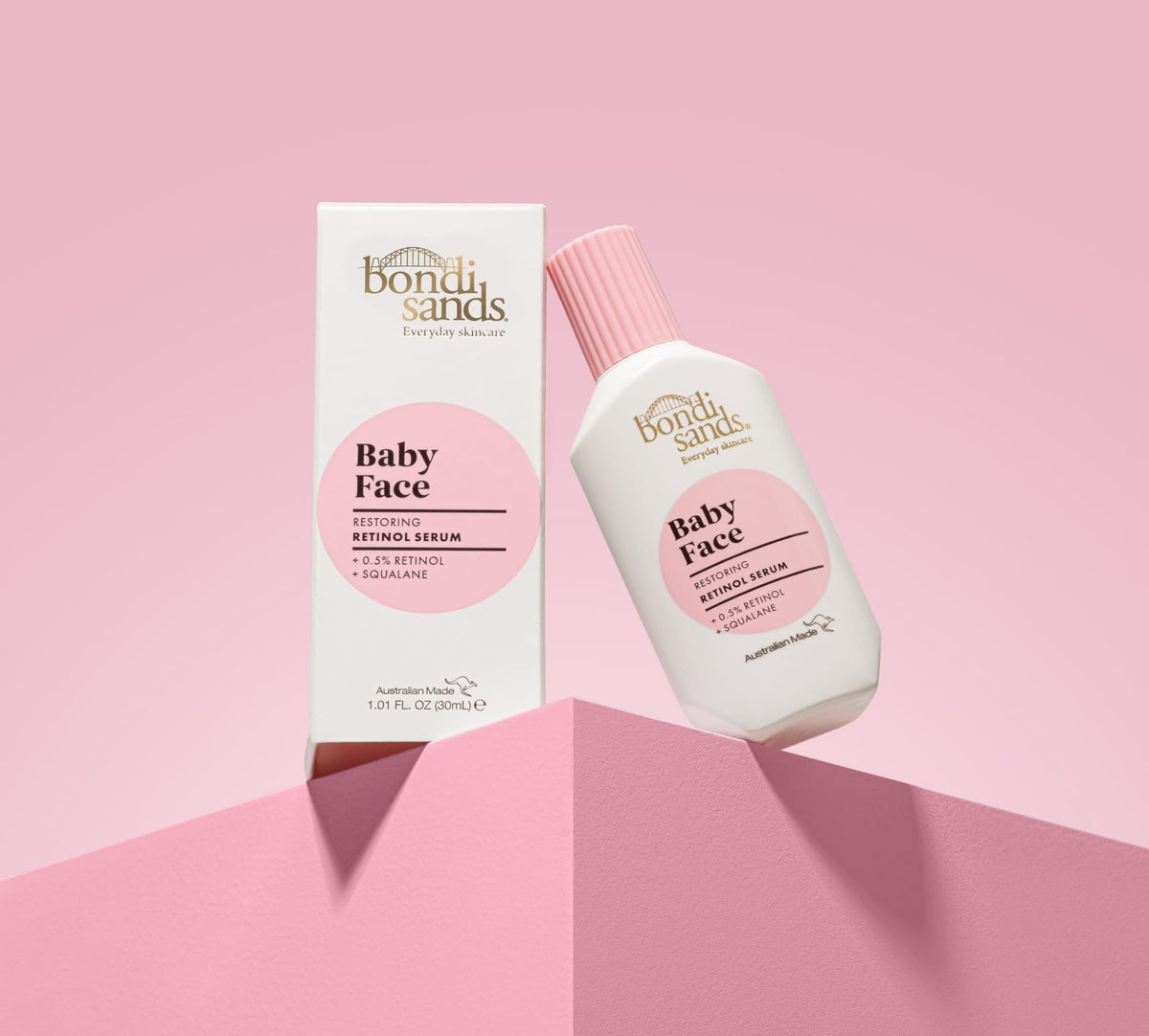 A pink and white bottle of BondiSandsEU Baby Face Retinol Serum sits beside its matching box on a pink surface and background—formulated to help reduce fine lines for youthful-looking skin.