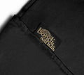 A close-up of black fabric features a stitched black label reading "BondiSandsEU" in gold. The Self Tanning Pillow Protector is sewn onto a folded corner, ensuring mess-free tanning and preventing tan transfer.